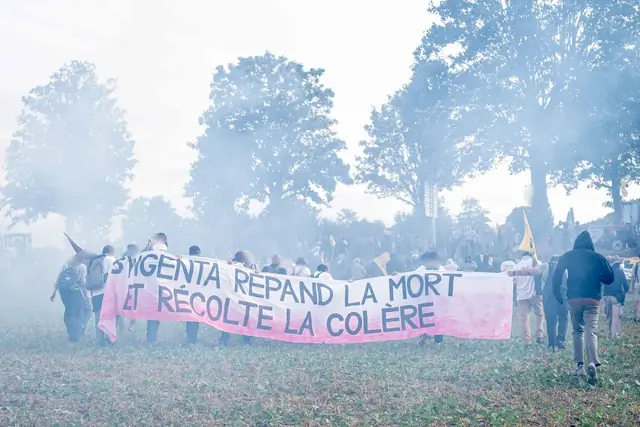 The banner “Syngenta spreads death and reaps anger” (“Syngenta répand la mort et récolte la colère”) in a cloud of tear gas