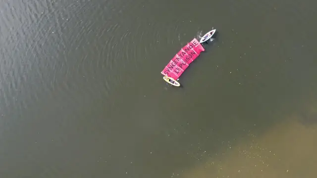 Aerial view of kayaks towing a pink floating banner on the Seine
