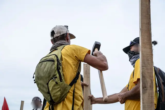 Two people in yellow T-shirts drive a stake into the field with a sledgehammer