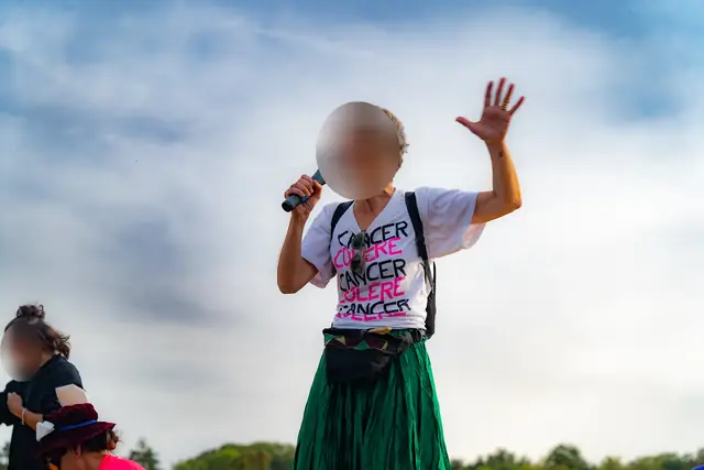A Cancer Colère activist speaks into the microphone, standing on a tractor’s flatbed trailer