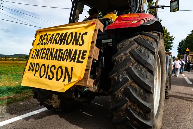 A tractor displays the banner “Let’s disarm the poison international” (“Désarmons l’internationale du poison”)