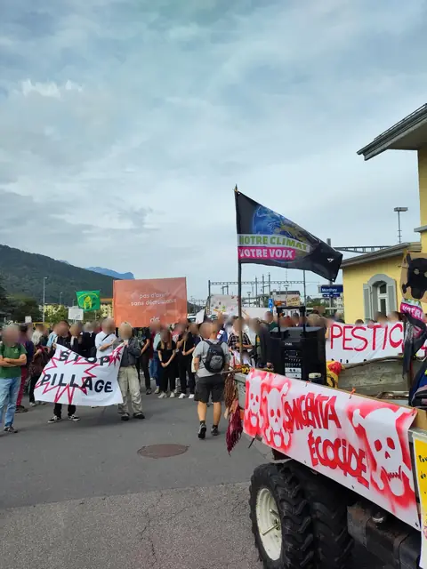 The march sets off from the station, with “Stop plunder” (“Stop pillage”) and “Syngenta ecocide” (“Syngenta écocide”) banners on a decorated vehicle