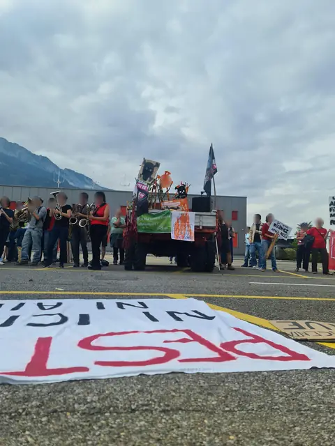 The brass band plays outside the factory, behind the banner spread on the ground