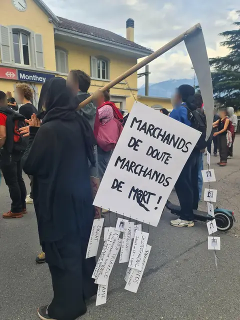 A person dressed as the Grim Reaper carries a sign reading “Merchants of doubt, merchants of death!” (“Marchands de doute, marchands de mort !”) outside the station