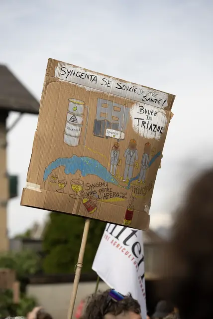 A hand-drawn sign: “Syngenta cares about your health: drink triazole!” (“Syngenta se soucie de votre santé : buvez du triazole !”)