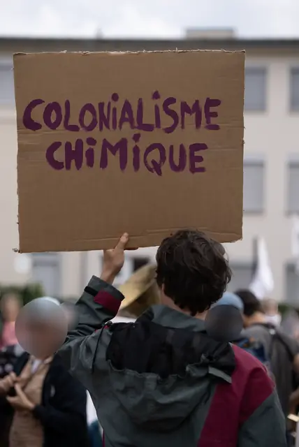 A cardboard sign reading “Chemical colonialism” (“Colonialisme chimique”) raised above the crowd